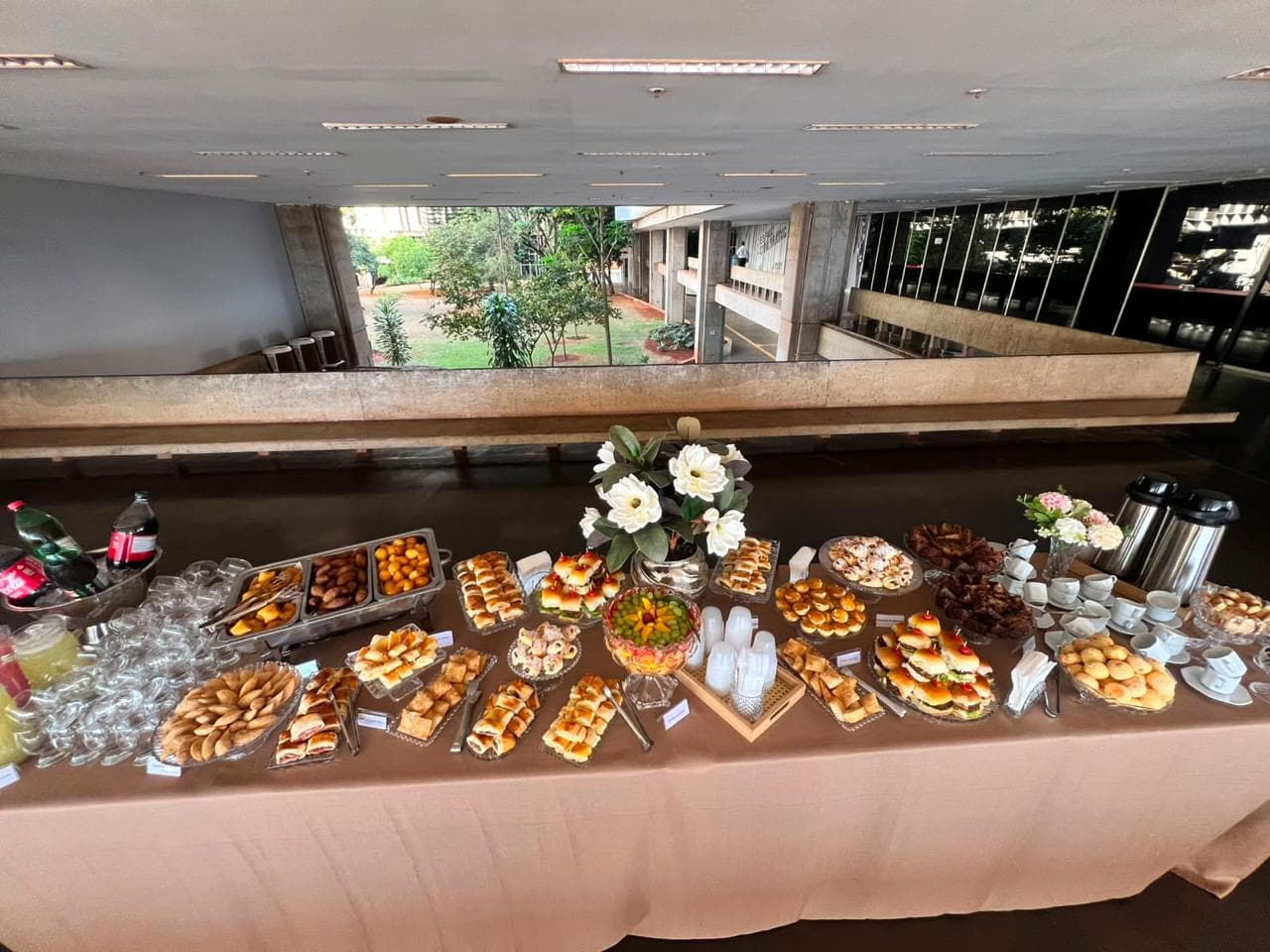 Mesa de buffet montada em toda a extensao de um salao com vista para o jardim