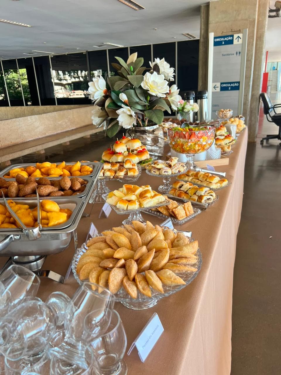 Mesa com toalha rose, pasteis, folhados e arranjo de magnolias brancas