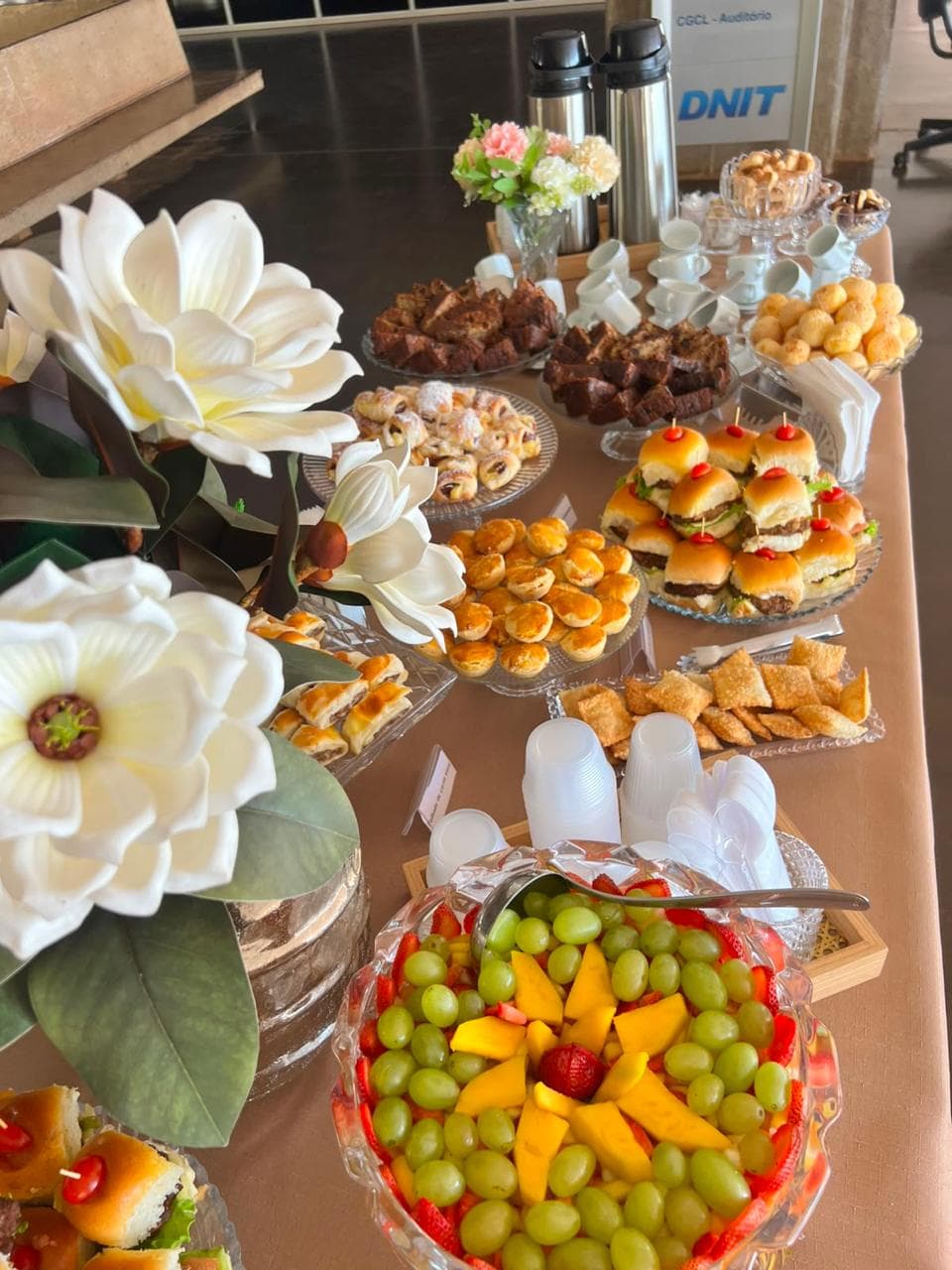 Mini hamburgueres, empadinhas e salada de frutas em mesa de evento corporativo