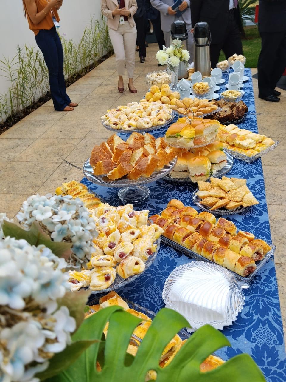 Mesa de coffee break em area externa com convidados ao fundo