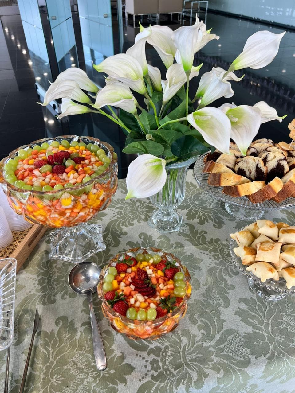 Duas tacas de cristal com salada de frutas ao lado de copos de leite e bolo marmore