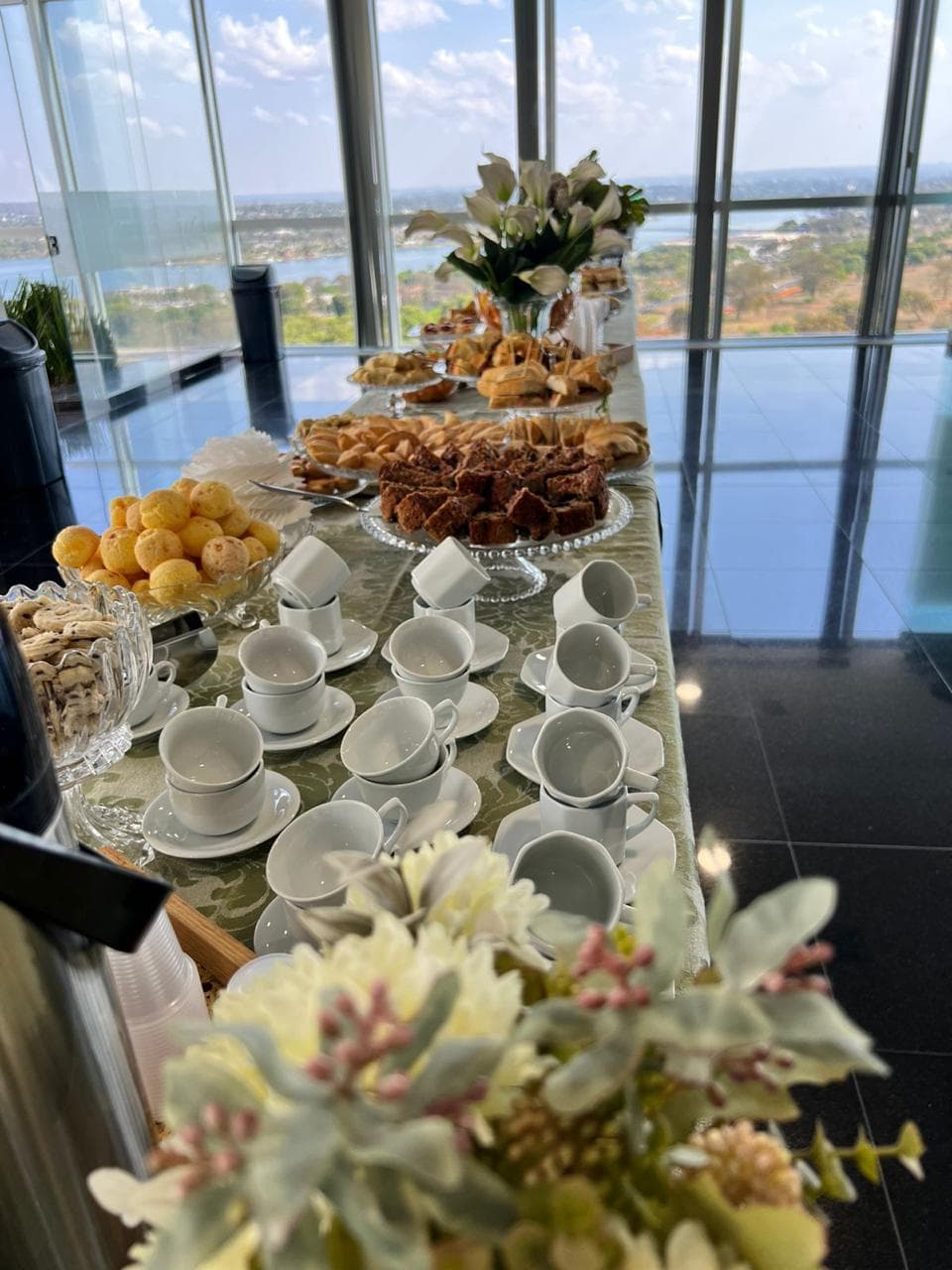 Xicaras de porcelana, pao de queijo e bolos em mesa com vista panoramica