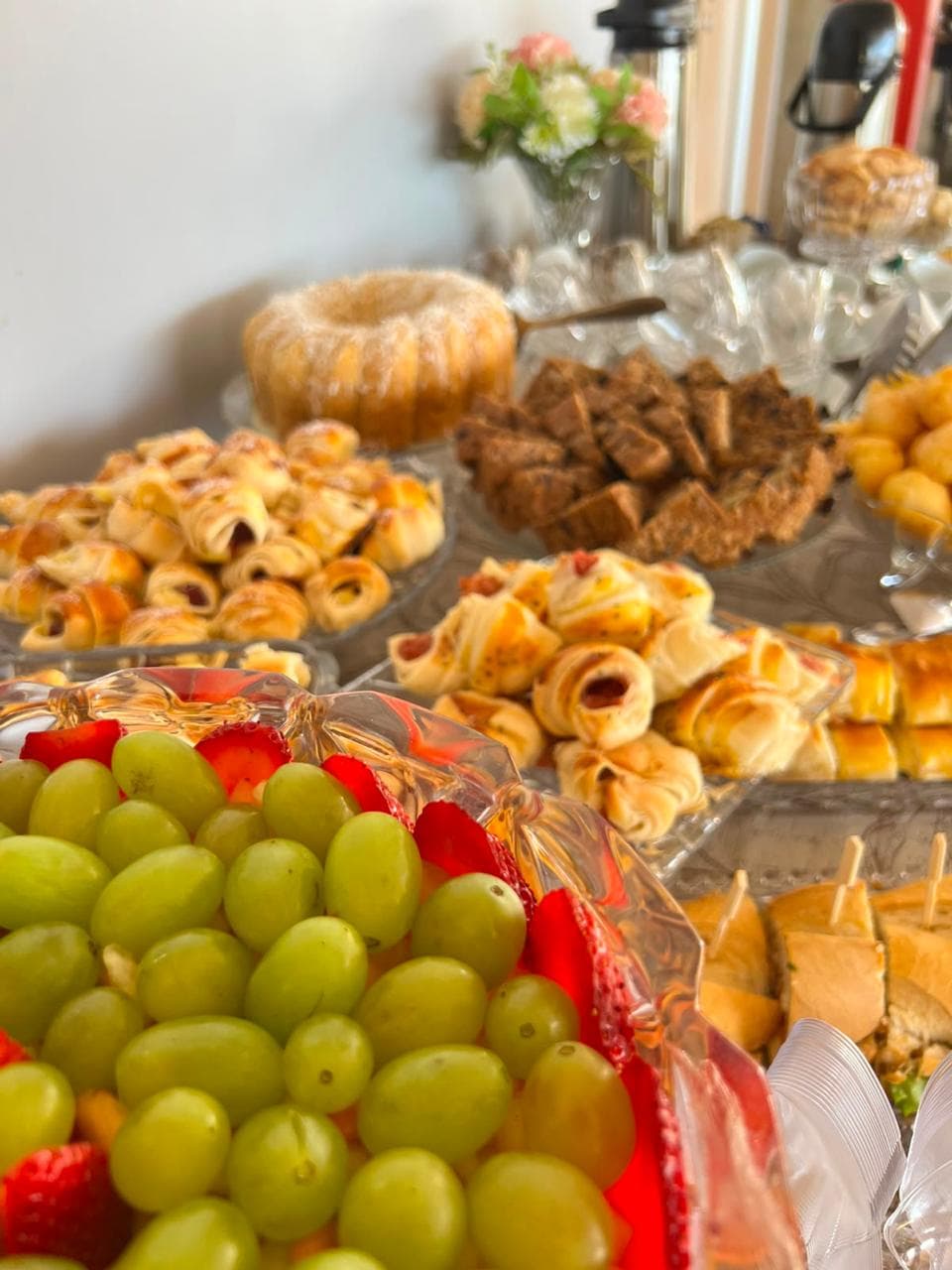 Detalhe de bolo, enroladinhos e salada de frutas em travessas de cristal