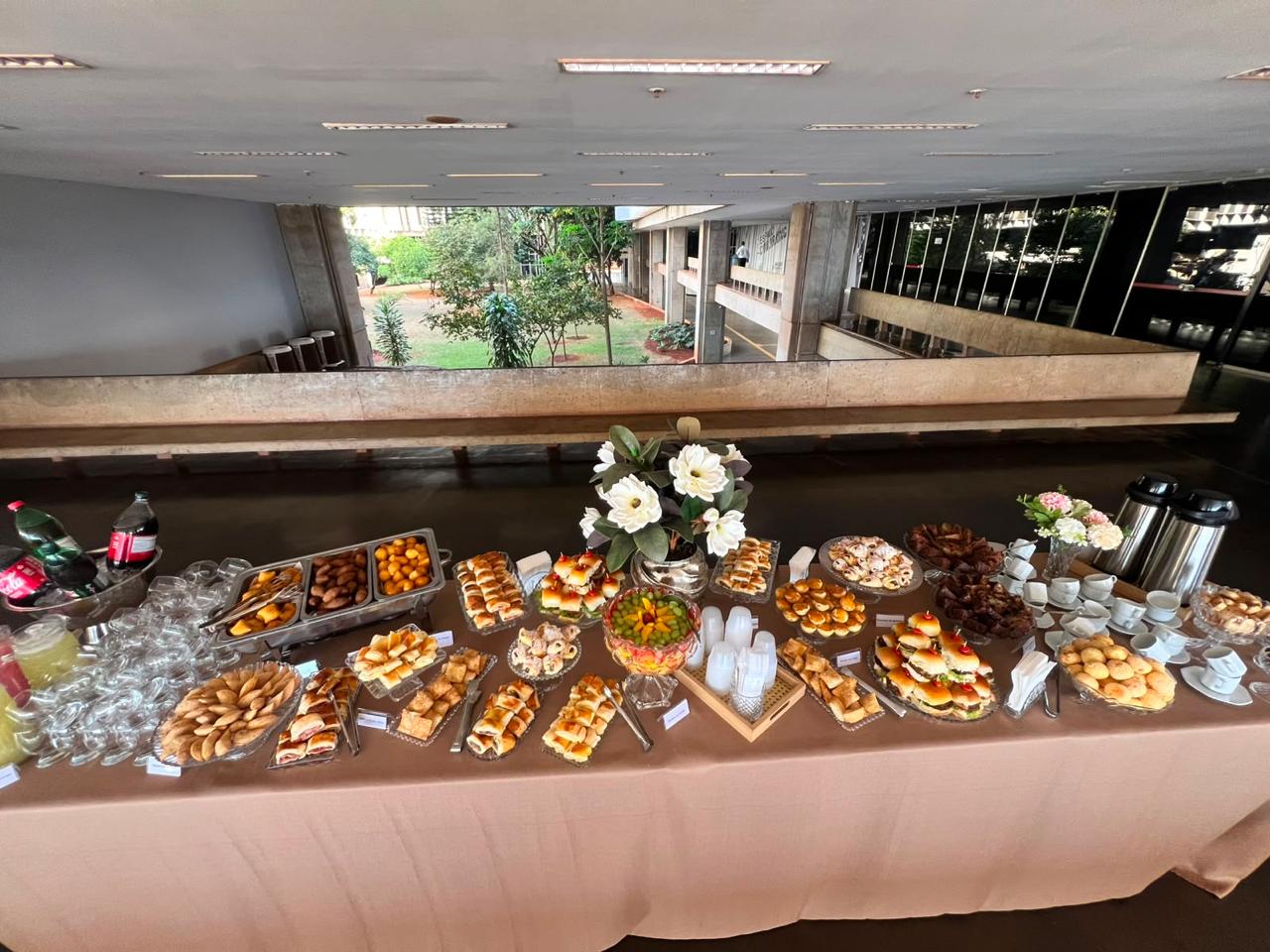 Mesa de buffet montada em toda a extensao de um salao com vista para o jardim